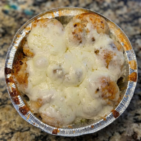 Cheesy garlic knots in a foil pan, with melted mozzarella cheese bubbling over golden-brown dough.