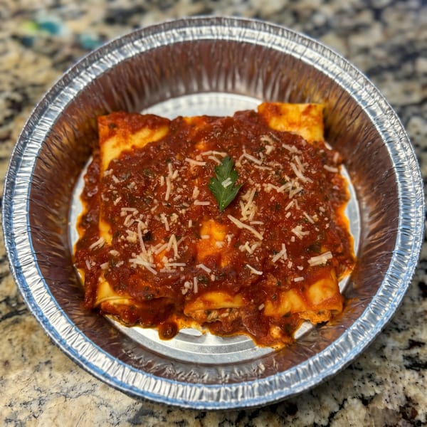 Baked cannelloni pasta with red sauce, parmesan cheese, and a parsley garnish in a foil pan.