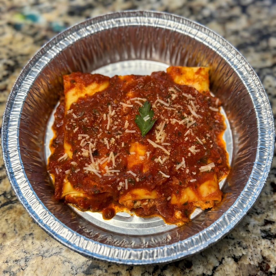 Baked cannelloni pasta with red sauce, parmesan cheese, and a parsley garnish in a foil pan.